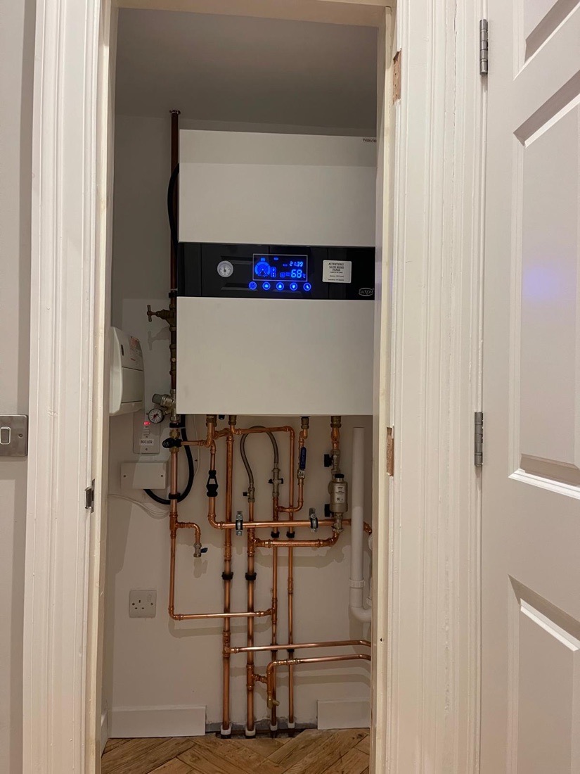 A Navien combi boiler installed in a hallway cupboard above a herringbone wood floor